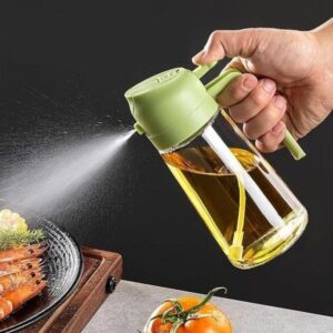 A hand holds a green oil sprayer misting oil over a plate of shrimp.